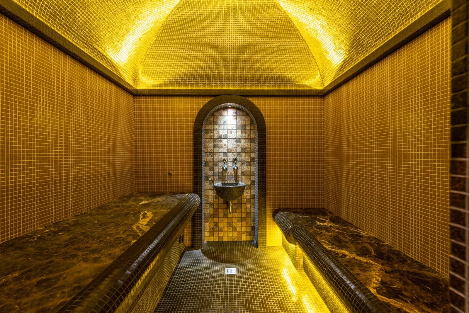 Hammam voûté en mosaïque dorée avec banquettes en marbre et fontaine