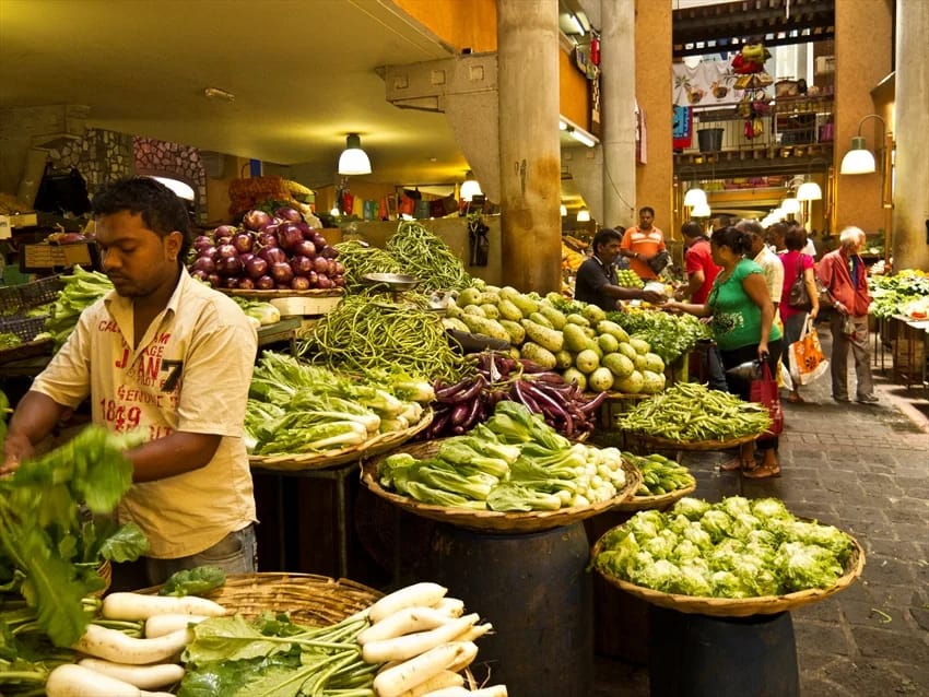 Marchand de légumes devant ses étals dans un marché de Port-Louis