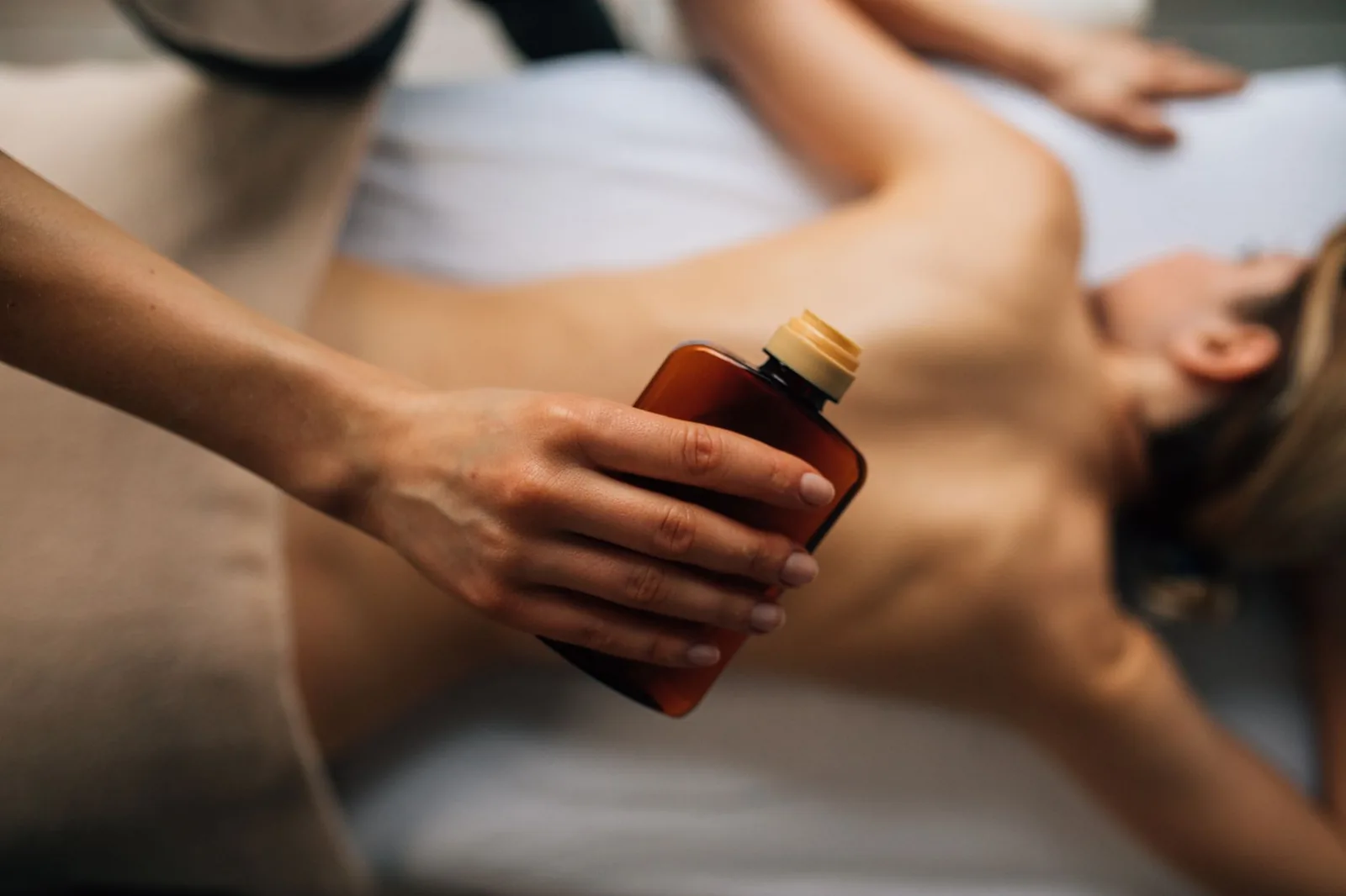 Thérapeute versant de l'huile de massage sur le dos d'une cliente en cabine de spa