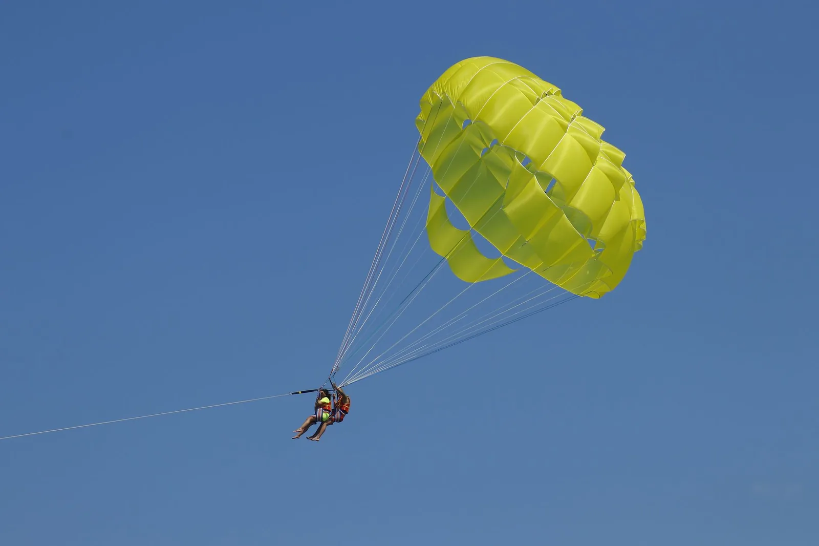 Parachute ascensionnel jaune tracté par un bateau dans un ciel bleu