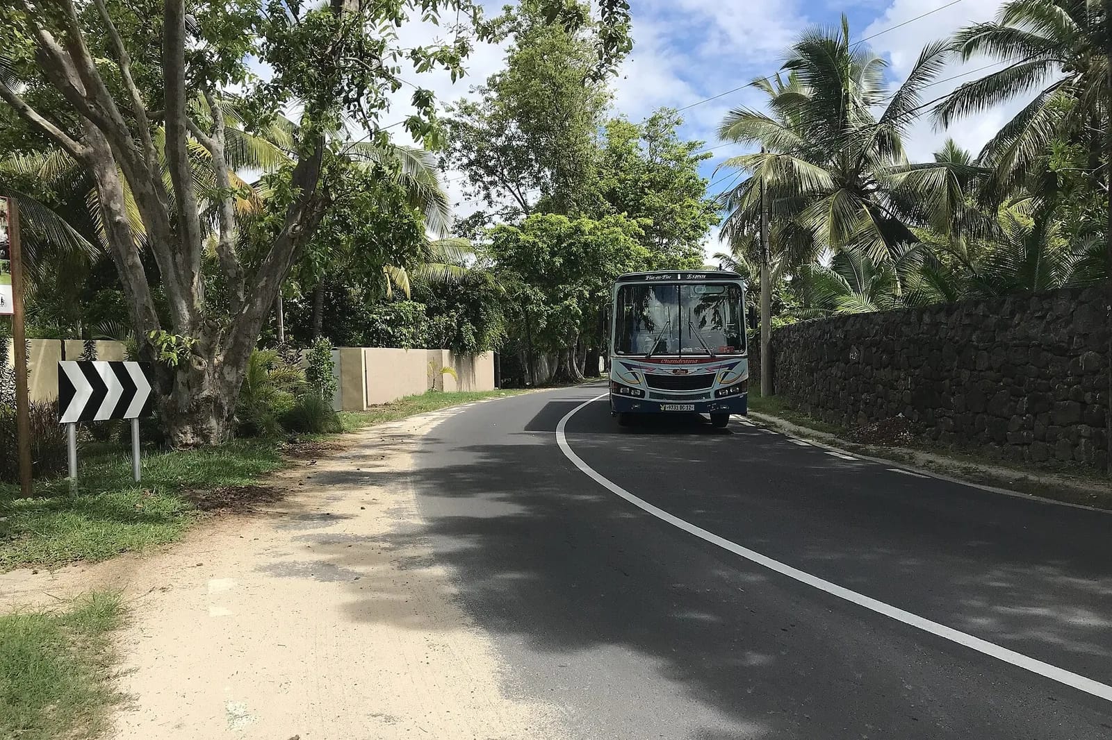 Bus local sur une route bordée de palmiers et d'un mur de pierre à Flic-en-Flac, île Maurice