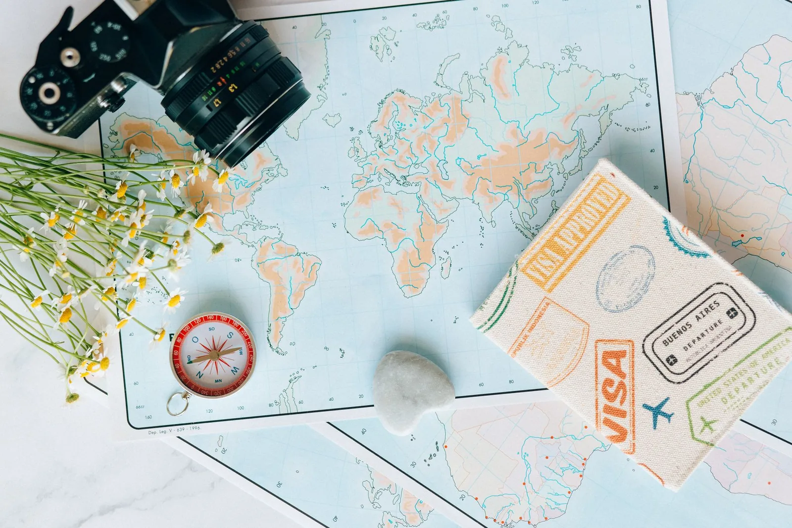 Cartes du monde, boussole, appareil photo et passeport tamponné posés à plat sur une table