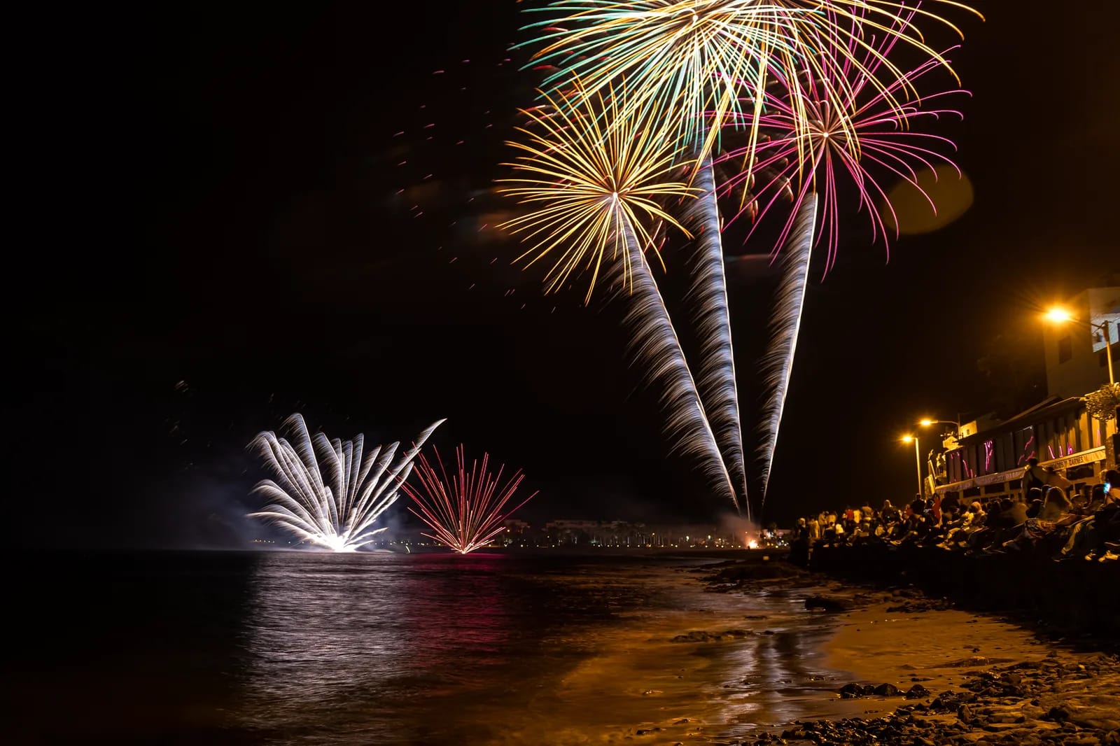 Feux d'artifice de nuit au-dessus d'une baie, foule rassemblée sur le front de mer