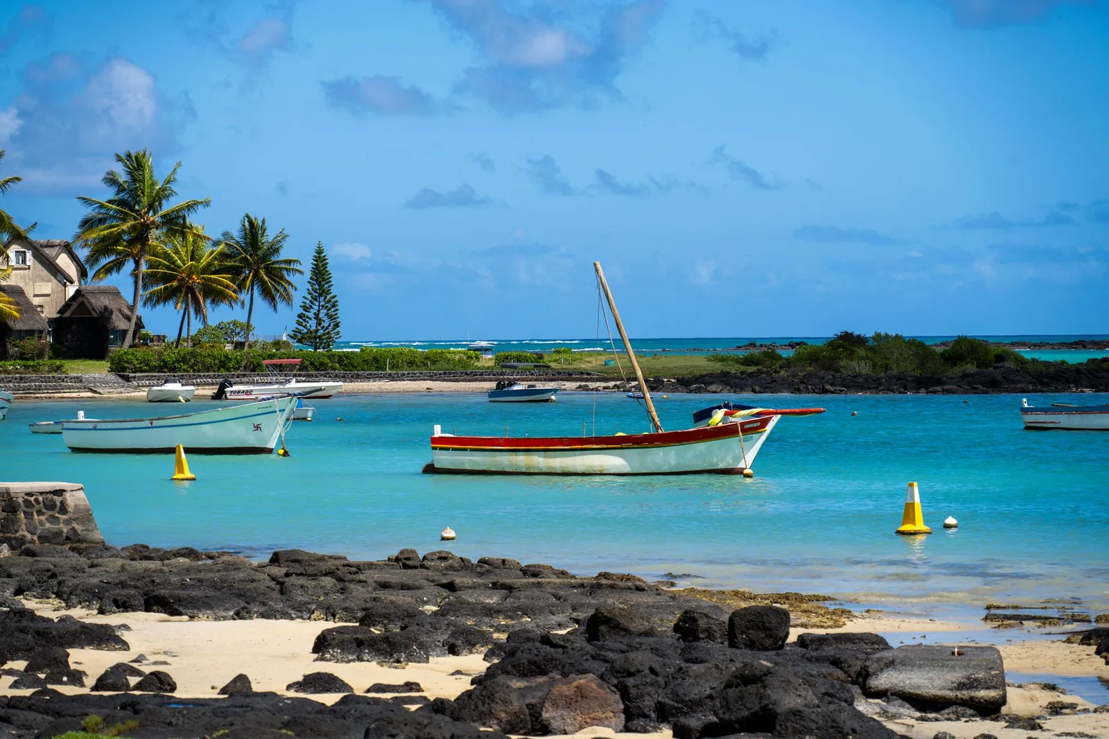 Barques sur une mer turquoise calme, palmiers et rochers noirs sur la côte nord de l'île Maurice