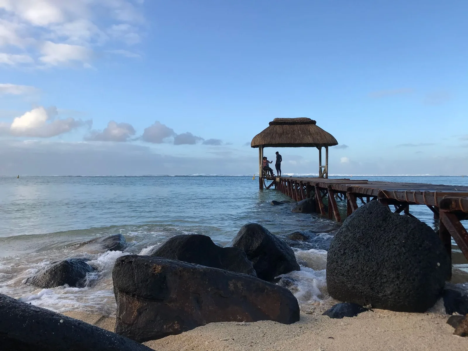 Ponton à toit de chaume et rochers volcaniques sur une plage de l'île Maurice, mer calme