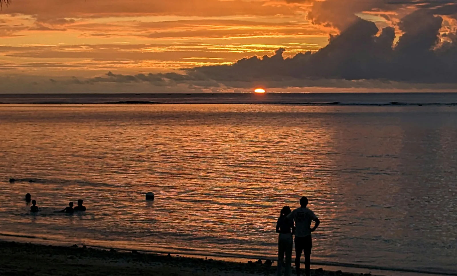 Coucher de soleil orange sur l'océan Indien depuis la plage de Flic en Flac, avec deux promeneurs, île Maurice
