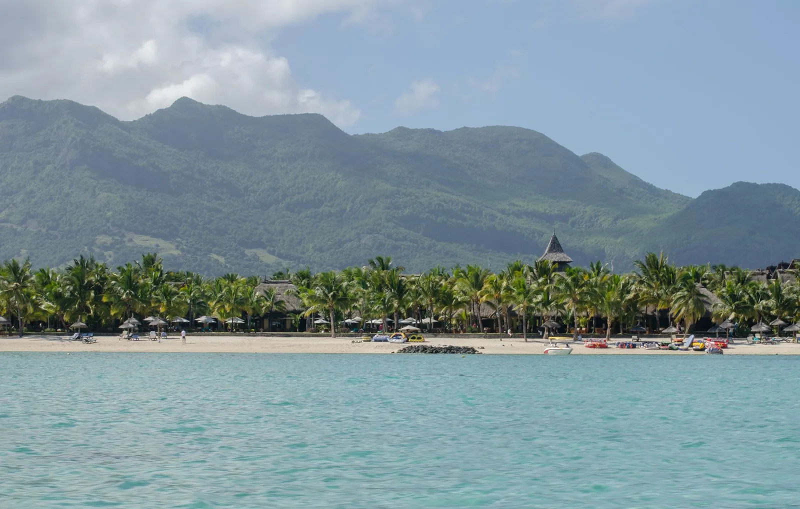 Plage bordée de palmiers devant les montagnes de l'ouest de Maurice