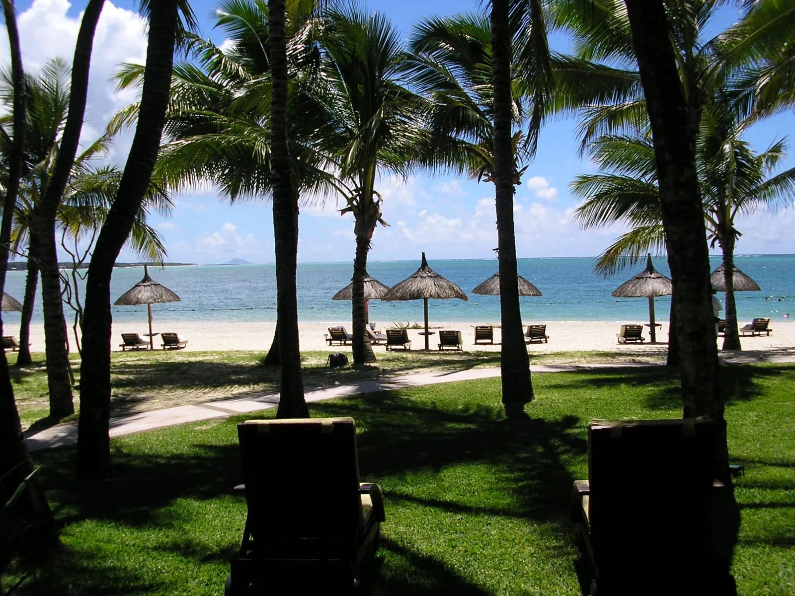 Plage de l'hôtel Le Saint Géran à Maurice : parasols de paille, transats et cocotiers face au lagon